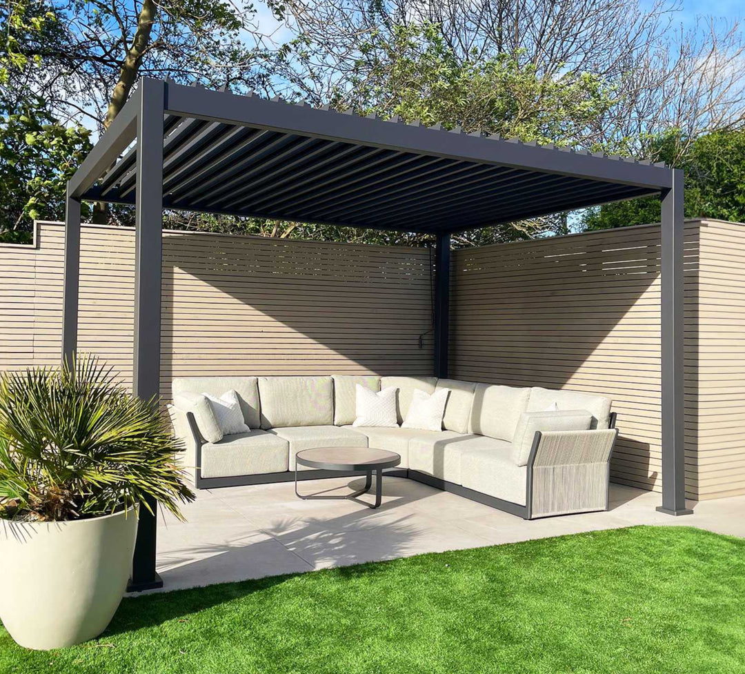Nova Titan Pergola Grey 4M x 3M with louvers open on a white slabbed patio with beautiful light grey roped sofa and plant to left corner.