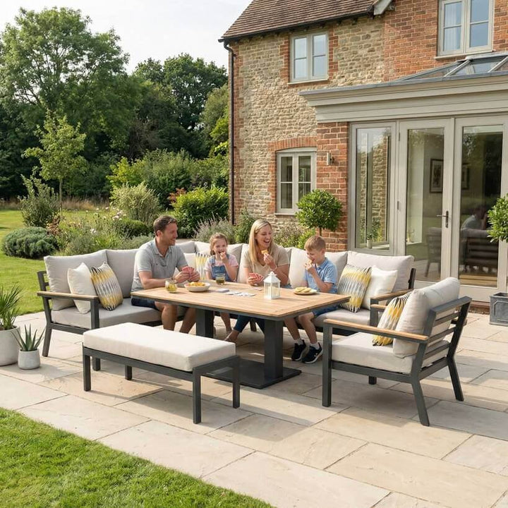 Nova Heidi outdoor living furniture set Midland Garden Furniture with people enjoying in front of a Cotswold house with plants at the back. right hand corner sofa set with arm chair bench and rising table. 