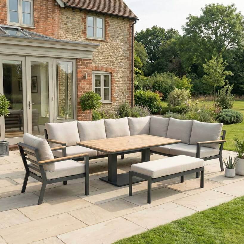 Nova Heidi outdoor living furniture set Midland Garden Furniture  in front of a Cotswold house with plants at the back. left hand corner sofa set with arm chair bench and rising table. 