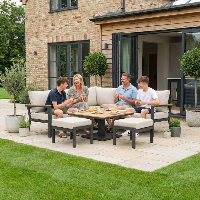 Nova Heidi outdoor living furniture set Midland Garden Furniture with people enjoying in front of a Cotswold house with plants at the back. corner sofa set. 