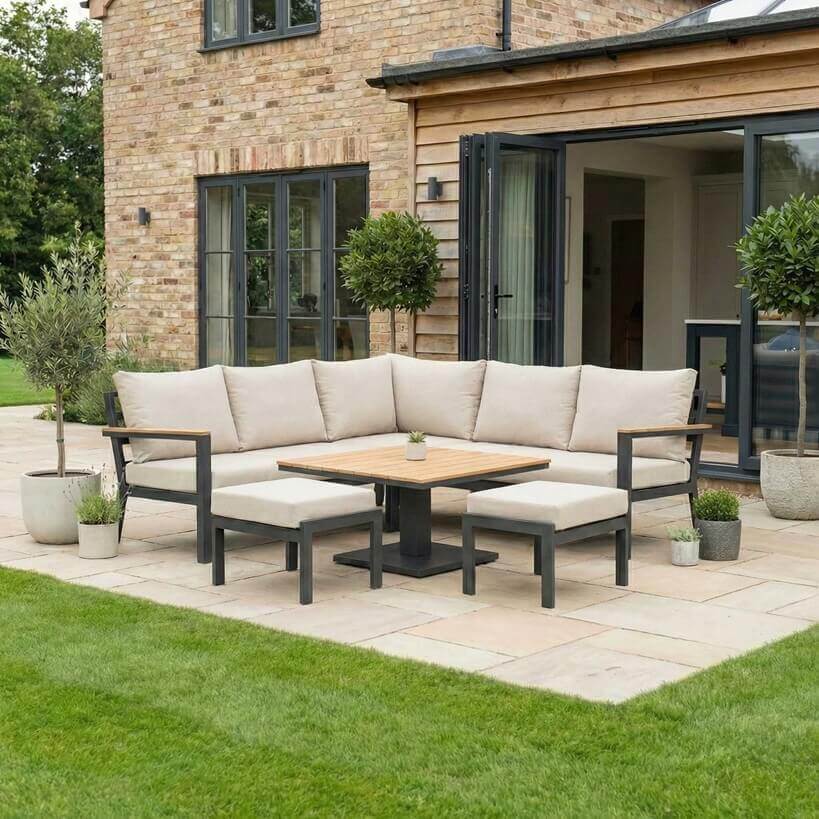 Nova Heidi outdoor living furniture set Midland Garden Furniture with people enjoying in front of a Cotswold house with plants at the back. corner sofa set with bench and rising table. 