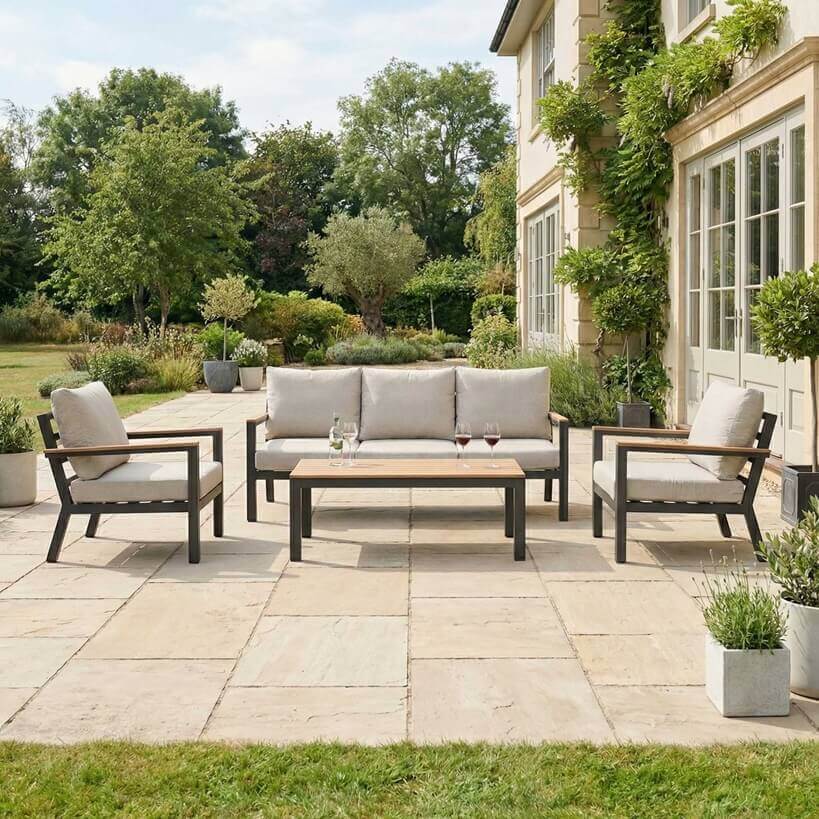 Nova Heidi outdoor living furniture set Midland Garden Furniture in front of a Cotswold house with plants at the back. 3 seater sofa and 2 arm chair set. 