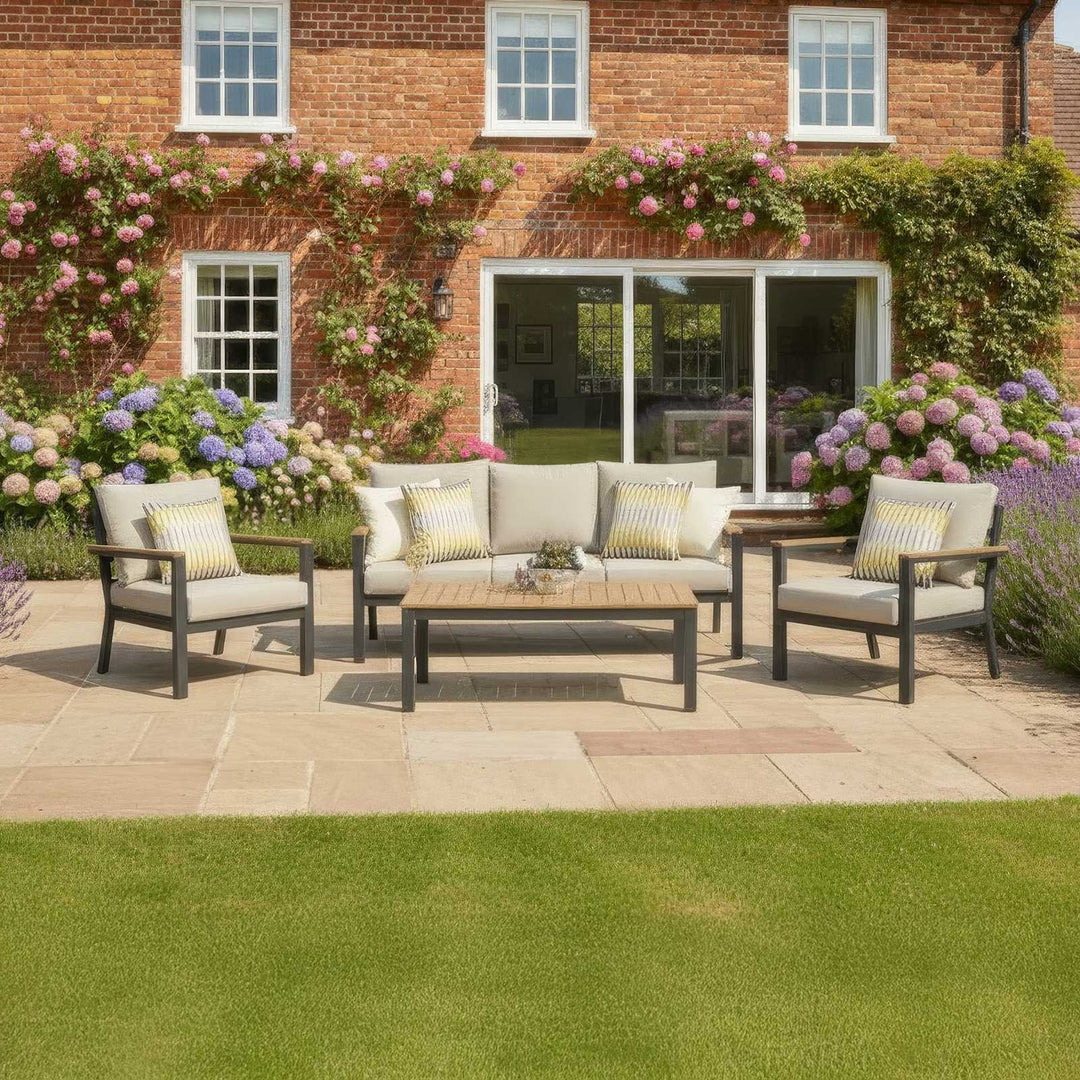 Nova Heidi outdoor patio set with furniture with 2 chairs and a 3 seat sofa in front of a brick house with floral decorations.