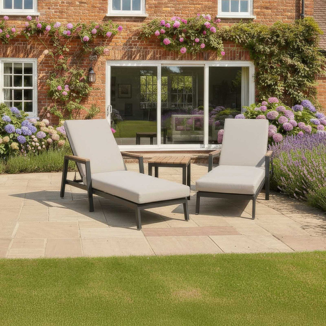 Two Nova Heidi sun lounger chairs on a patio with a garden and house in the background with flowers both sides and to the back