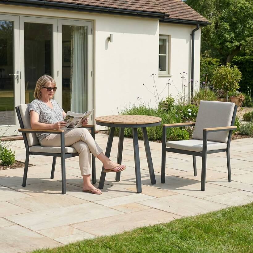 Nova Heidi outdoor living furniture set Midland Garden Furniture with people enjoying in front of a Cotswold house with plants at the back.2 seat bistro set with lady reading news paper