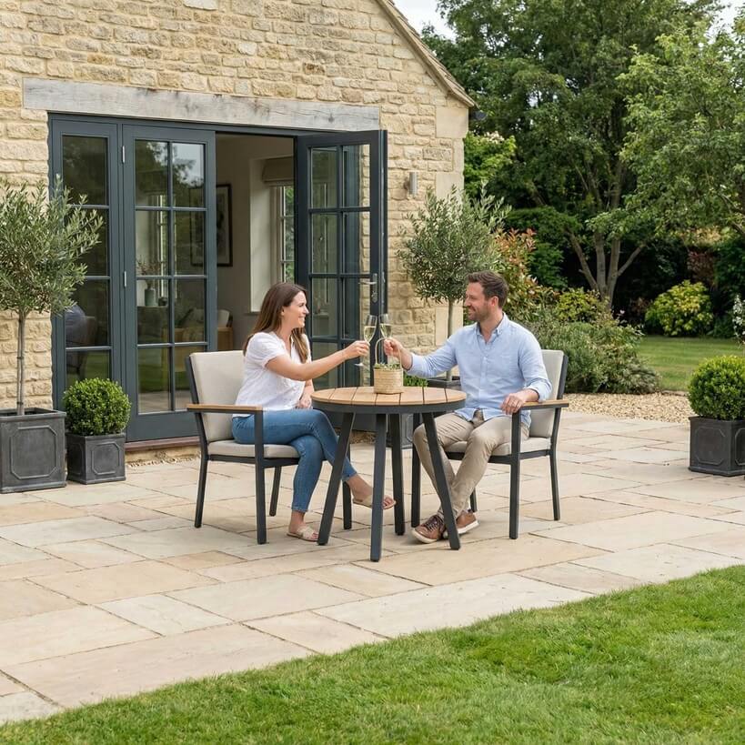 Nova Heidi outdoor living furniture set Midland Garden Furniture with people enjoying in front of a Cotswold house with plants at the back. 2 seater bistro set. 