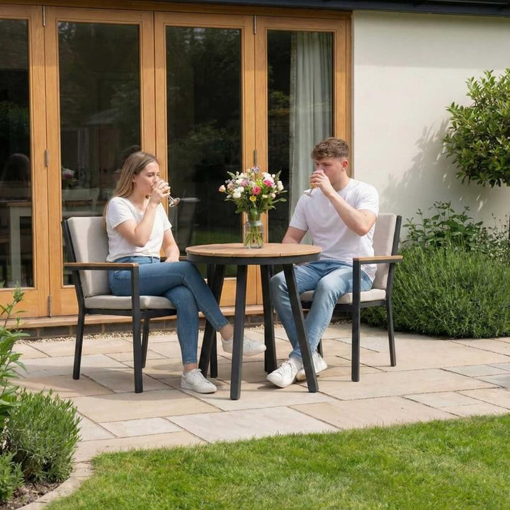 Nova Heidi outdoor living furniture set Midland Garden Furniture with people enjoying in front of a Cotswold house with plants at the back. 2 seater bistro set. 
