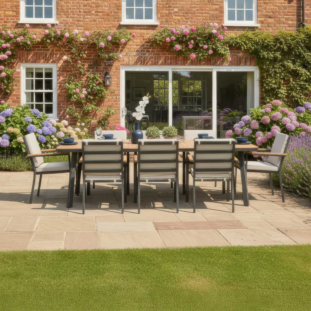 Nova Heidi 8 seater garden dining set rectangular table in back garden with wooden table top and grey aluminium frames, chairs with pebble/beige cushions. In garden with flowers and roses.