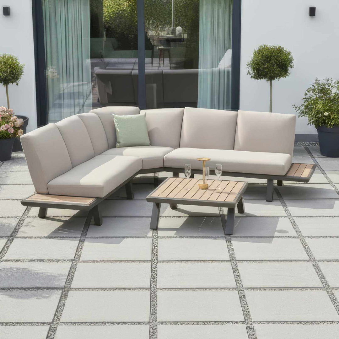 Nova Hunter outdoor living furniture set with a sectional sofa, rising table, and ottomans on a white background with modern white house behind and tiled floor.