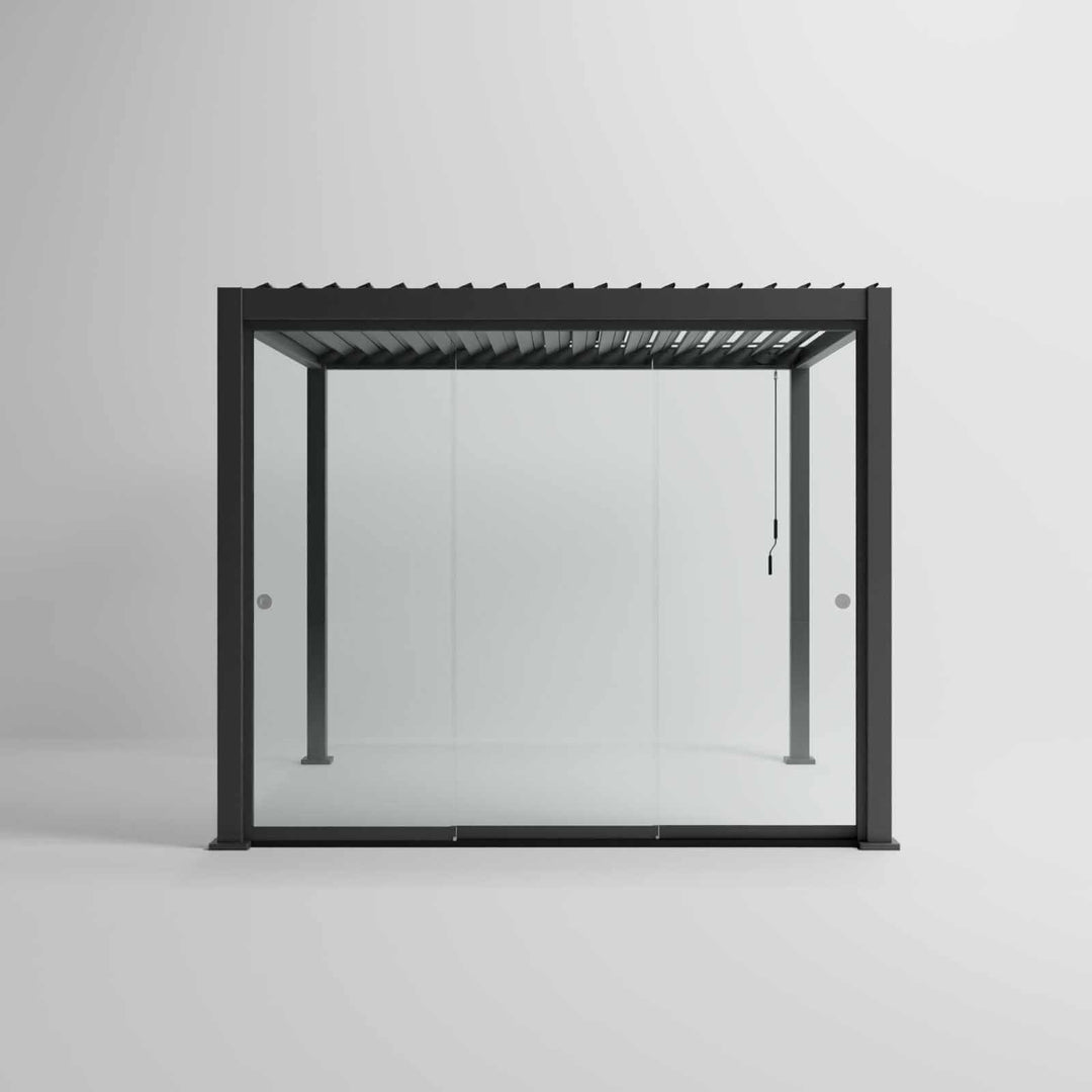 Nova Titan Pergola with glass sliding doors around the sides, with adjustable louvered roof. in anthracite grey with winder handle in pure white room. Front on shot angle.