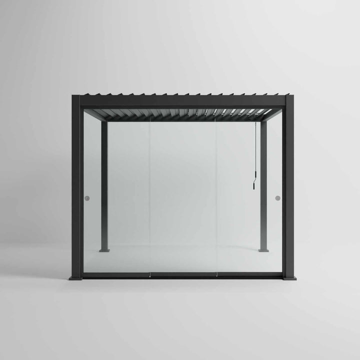 Nova Titan Pergola with glass sliding doors around the sides, with adjustable louvered roof. in anthracite grey with winder handle in pure white room. Front on shot angle.
