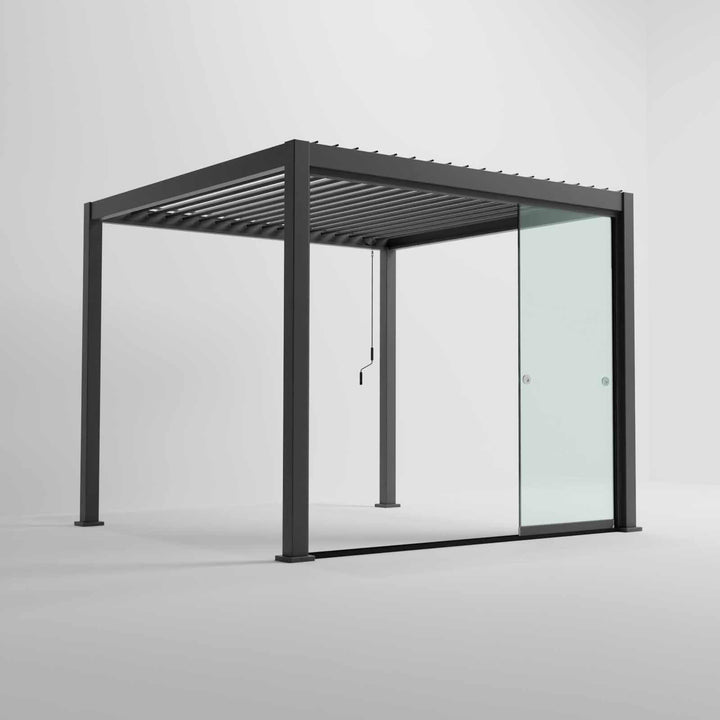 Nova Titan Pergola with glass sliding doors around the sides, with adjustable louvered roof. in anthracite grey with winder handle in pure white room. Image at a right angle with doors slid open.