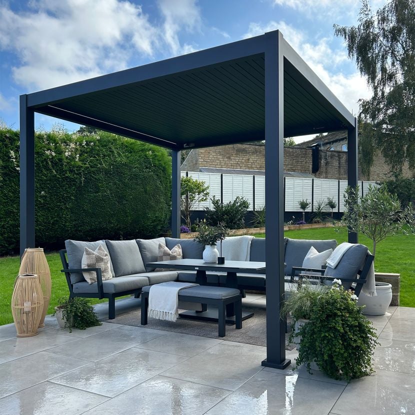 Nova Titan Plus in grey on modern light gey slabs on green lawn. with grey garden furniture under the Pergola and plant pots on each of the 4 corners