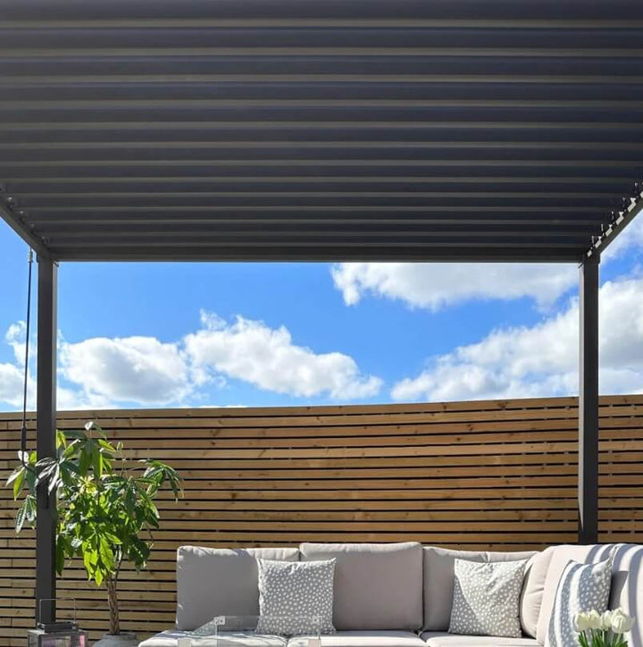 Outdoor patio with a Nova Luna pergola, wooden fence, and outdoor furniture under a clear blue sky.