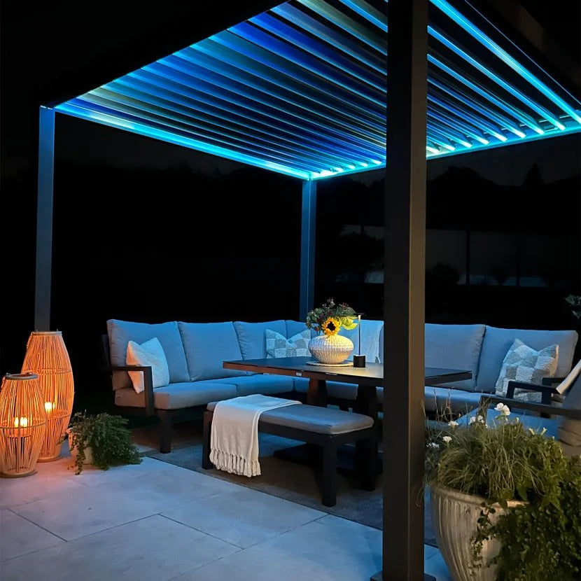 Outdoor patio with Nova Titan Pergola blue multi coloured LED lighting, garden furniture, and plants at night