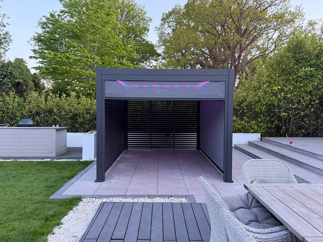 Nova Titan Pergola installation in Weybridge Surrey, by Midland Garden Furniture. External shot of the Pergola, with  privacy louvered walls that open and close and LED lighting system and beautiful patio with large white house behind.  front on shot.