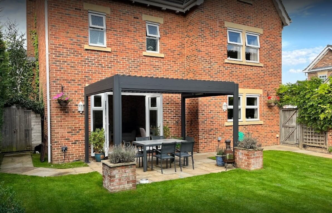 large brick new build house, with grey Aluminium Pergola in back garden, with green grass and 2 square brick pots with lavender in spring.