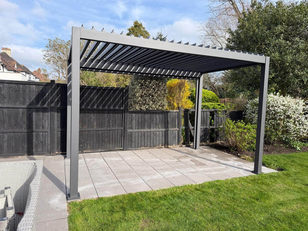Pergola structure in a garden setting with grass and trees in the background. Nova Titan Pergola 4M x 2.4M installation in Great Dalby, Leicestershire installed by Midland Garden Furniture. Patio area with a Grey pergola, outdoor furniture, and a garden view.