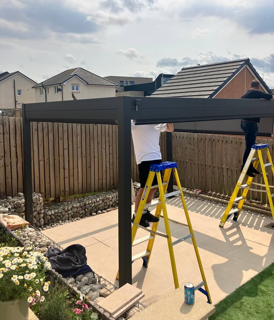 Two people installing a pergola in a backyard with houses in the background.