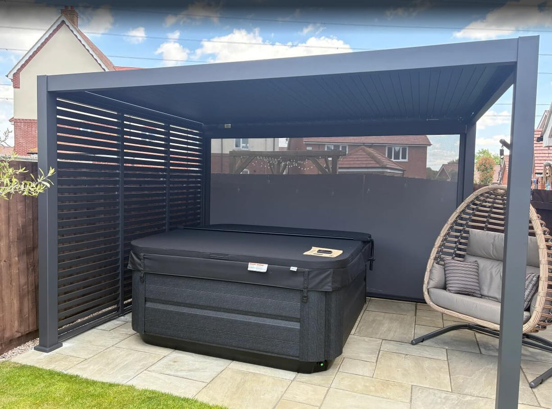 Black hot tub with egg chair and Aluminium Pergola in a back garden setting behind garage with new build houses in the background and privacy screen down at the back. Installed in Ripley, Derbyshire, UK.