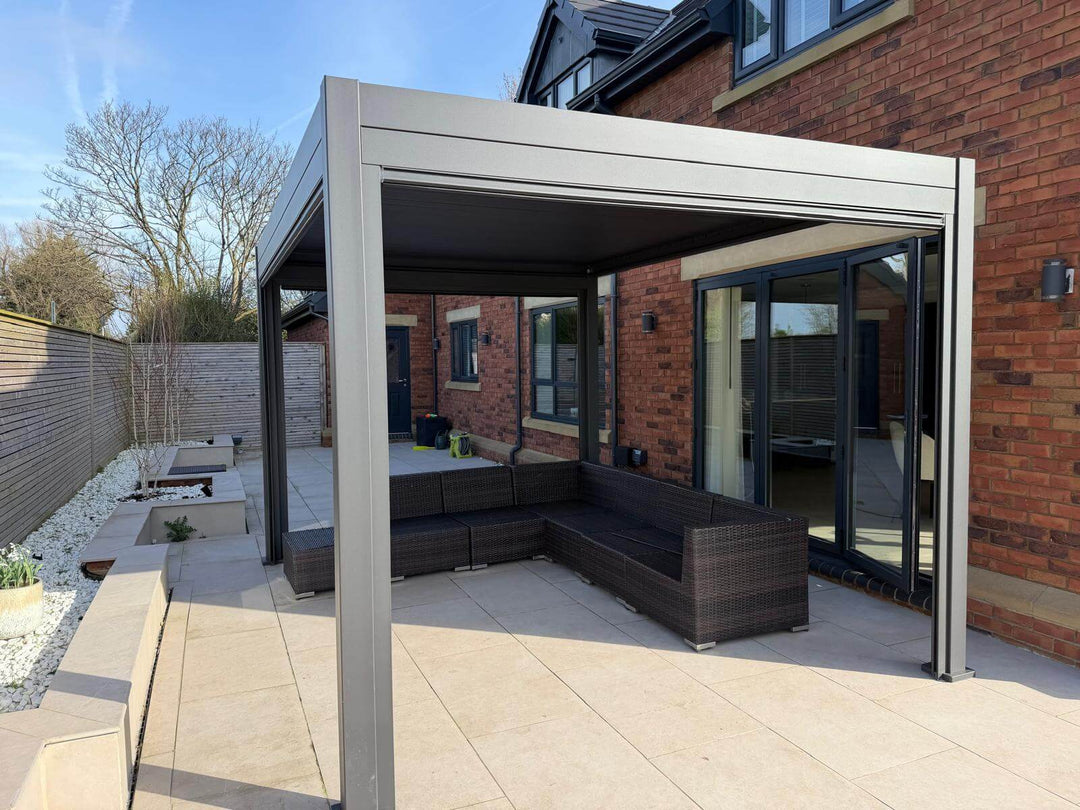 Outdoor patio area with a pergola and rattan sofa seating. Nova Titan Pergola Installation By Midland Garden Furniture Camberley, Surrey. In beautiful modern house rear garden with garden furniture underneath. Bright sunny day with wooden fence to the side.
