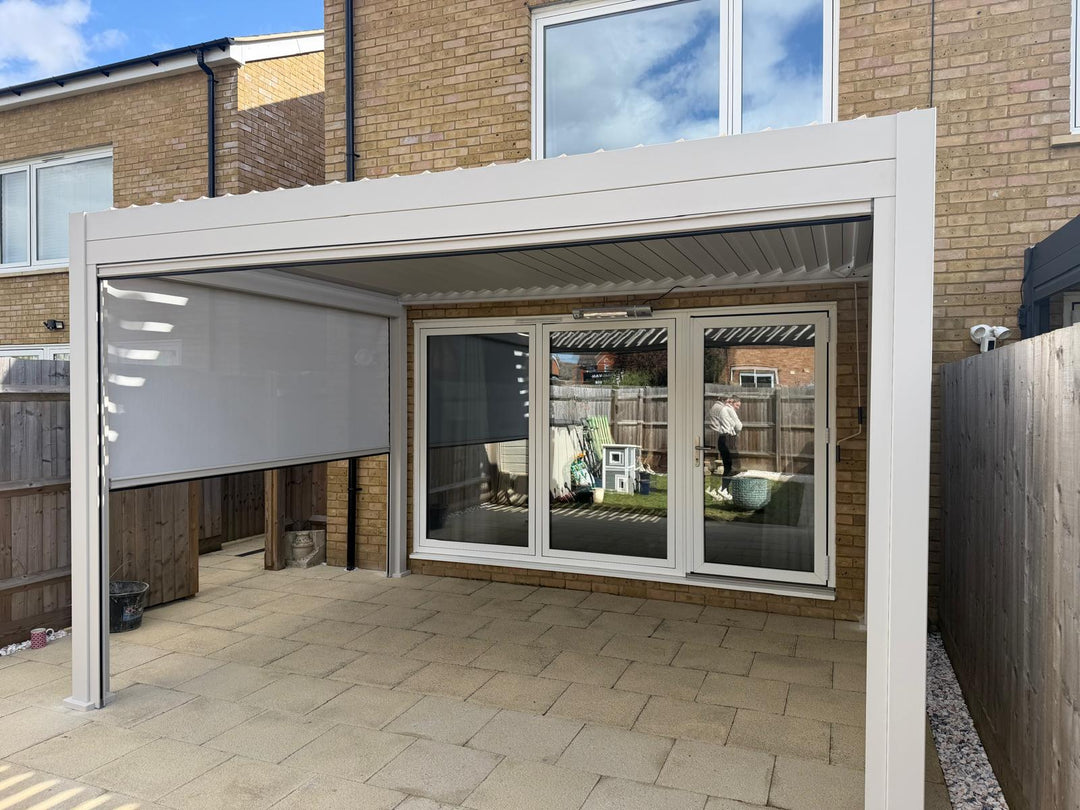 Patio area with a white pergola and sliding glass doors leading to a garden. Nova Titan Pergola Installation in Pebble in Melksham Wiltshire in a rear back garden, with louvered roof .