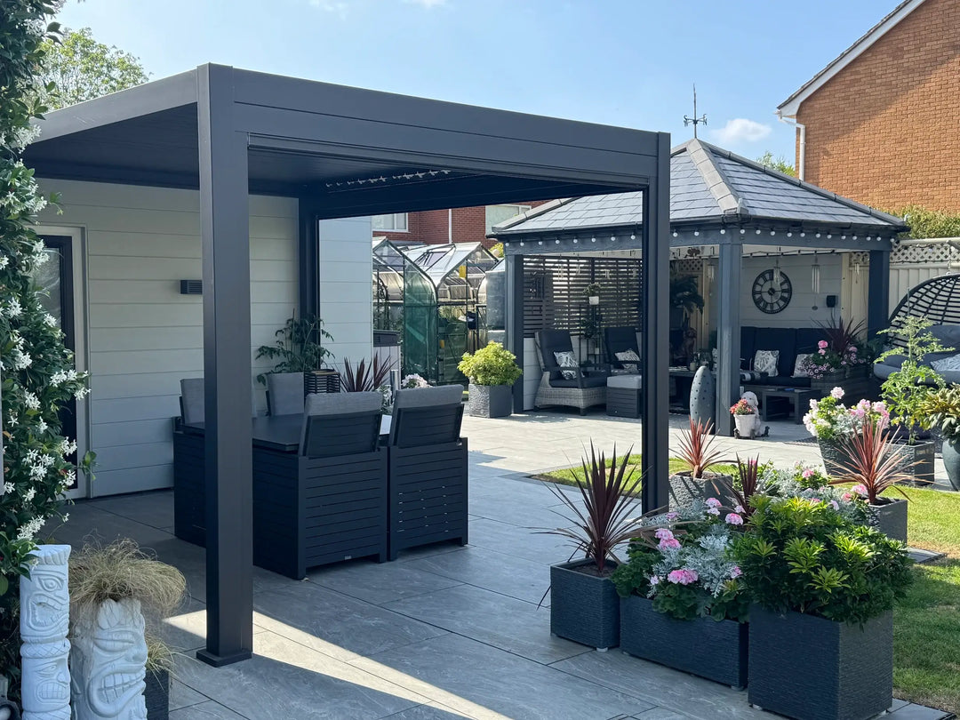 Nova Titan Pergola on large patio area with light grey slabs and grey garden furniture. in back garden with grey fence and 2 green house beyond. Installed in Ripley, Derbyshire, UK.