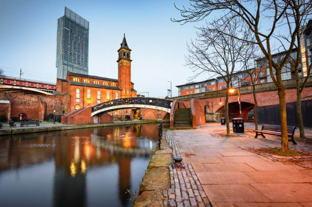 Pergola Installation Manchester, Depicted by Cityscape with a canal, bridge, and buildings under a clear blue sky.