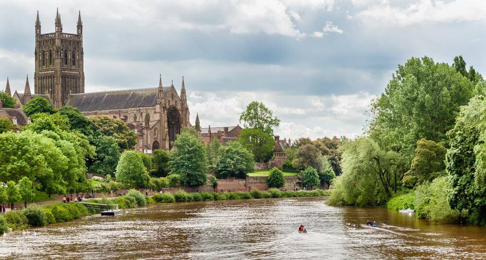 Pergola Installation Worcestershire, depicted by River flowing through a town with a large cathedral and greenery on a cloudy day.