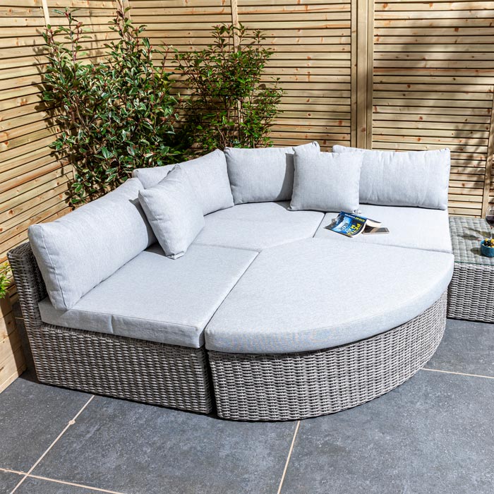 Rowlinson Marbella Multifunction Rattan Garden Furniture, with grey rattan and light grey cushions with a fence behind and bush at the back. Corner section image making a day bed.