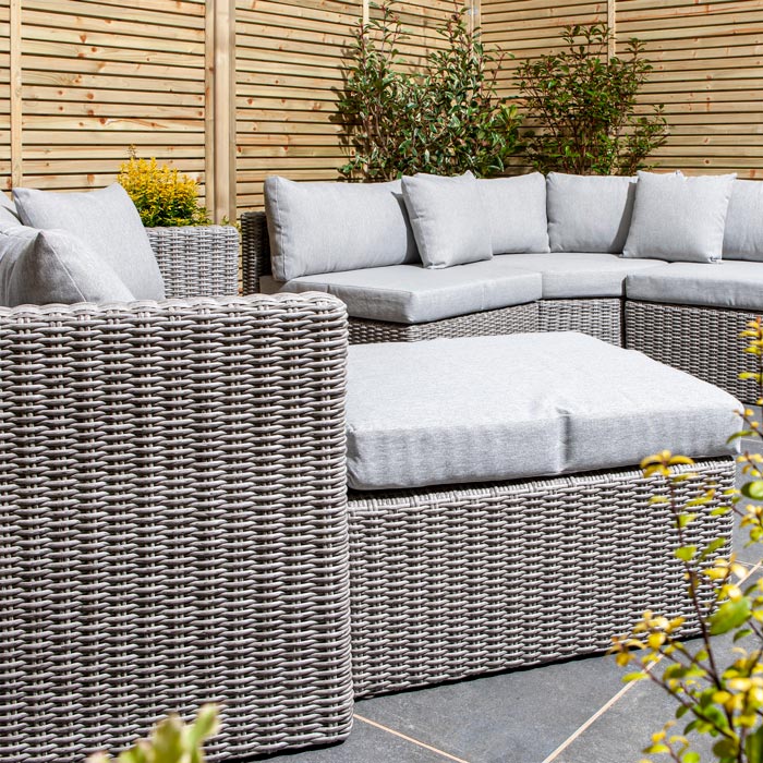 Rowlinson Marbella Multifunction Rattan Garden Furniture, with grey rattan and light grey cushions with a fence behind and bush at the back. Close up of foot stool.