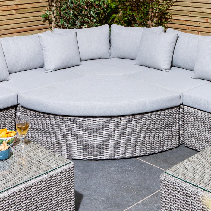 Rowlinson Marbella Multifunction Rattan Garden Furniture, with grey rattan and light grey cushions with a fence behind and bush at the back. Corner section image.